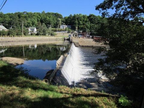 Water flowing over the Jay Hydro Dam, trees in the background and the right foreground.